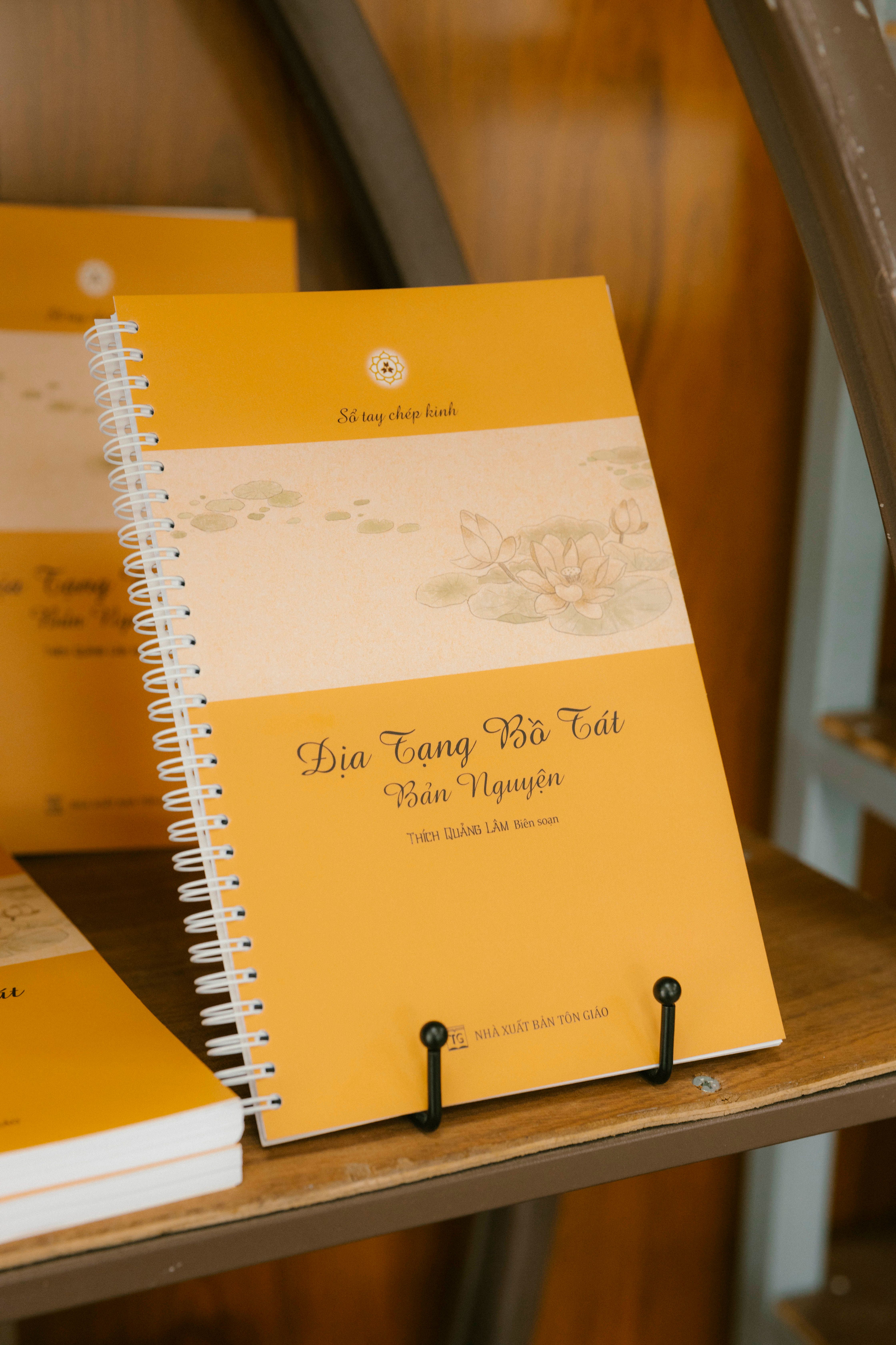 A yellow spiral notebook with floral design displayed on a wooden shelf.
