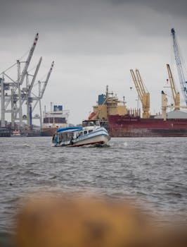 Vessel navigating through Hamburg port, showcasing cranes and cargo ships under an overcast sky.