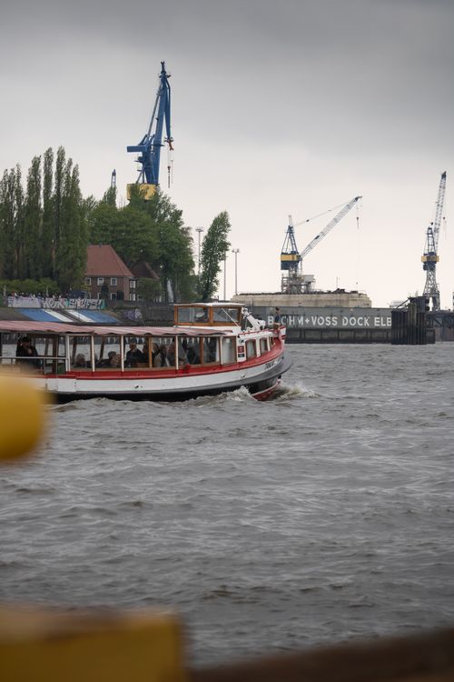 Free A ferry navigating through the industrial landscape of Hamburg harbor with cranes in the background. Stock Photo