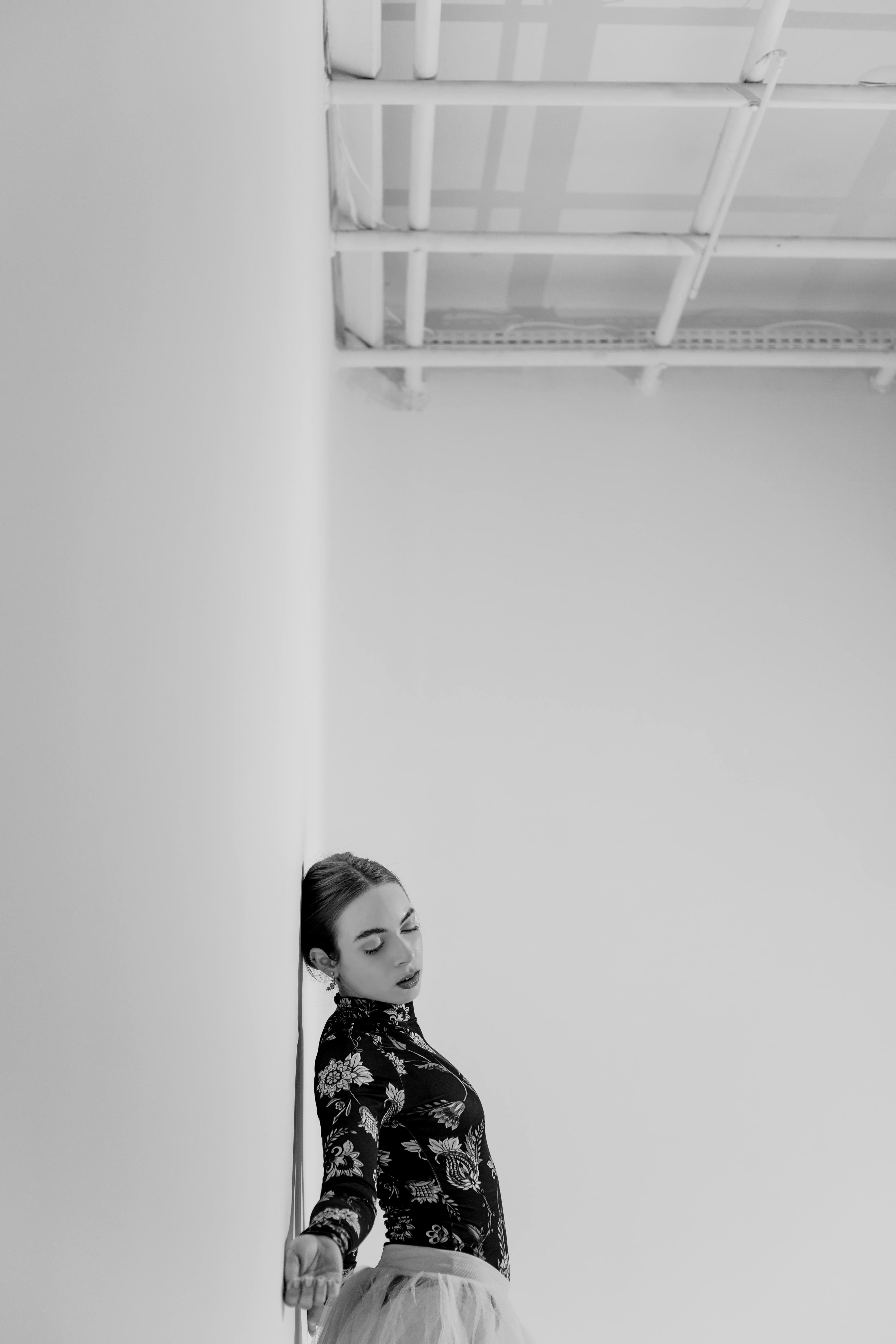 Black and white photo of a dancer leaning gracefully against a wall in a studio.