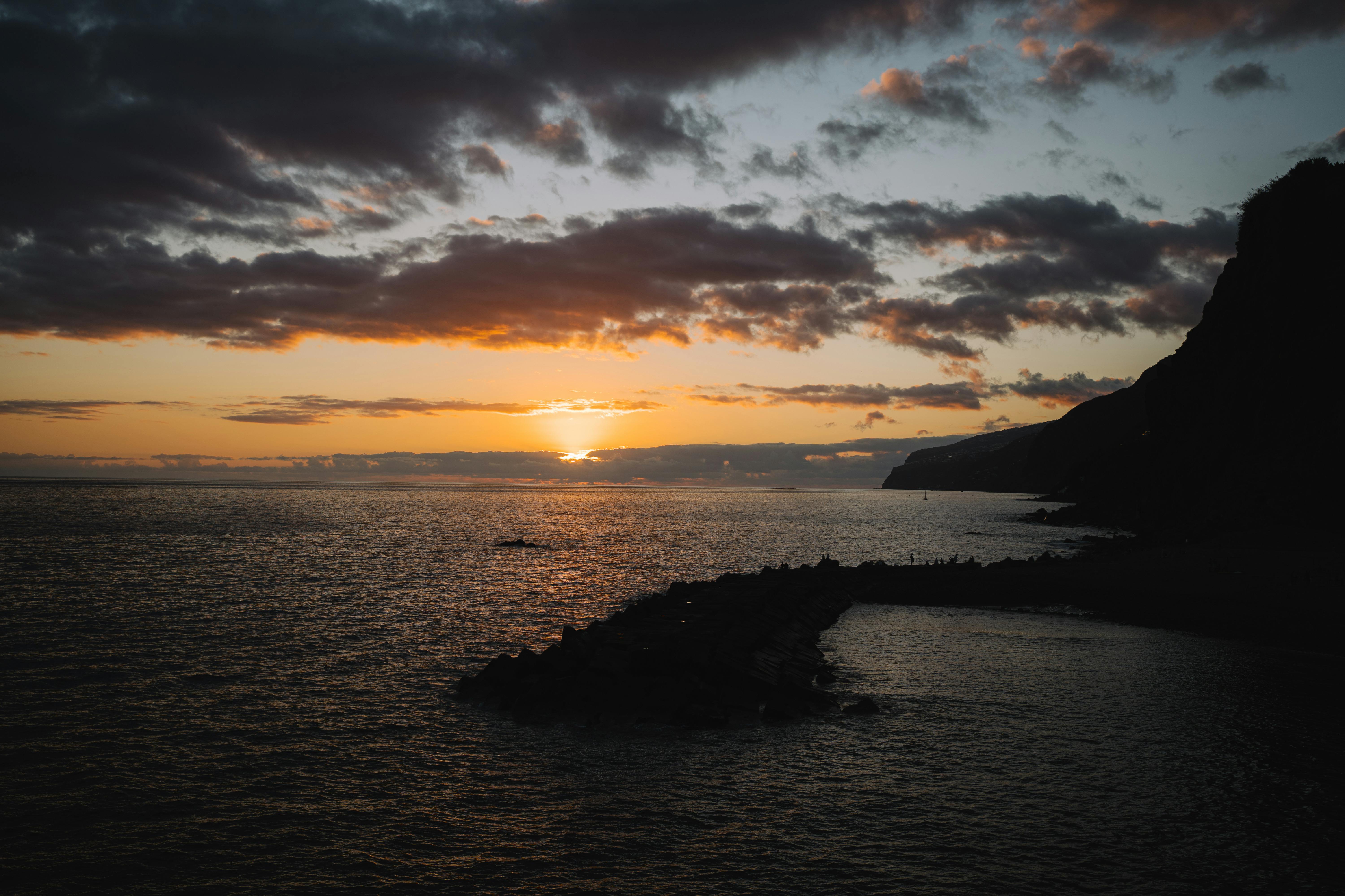 A breathtaking sunset view with silhouetted rocky coastline and vibrant sky reflections on the ocean.