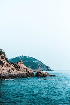 在晴朗的天空下，岩石海岸线与碧绿宁静的海洋相得益彰