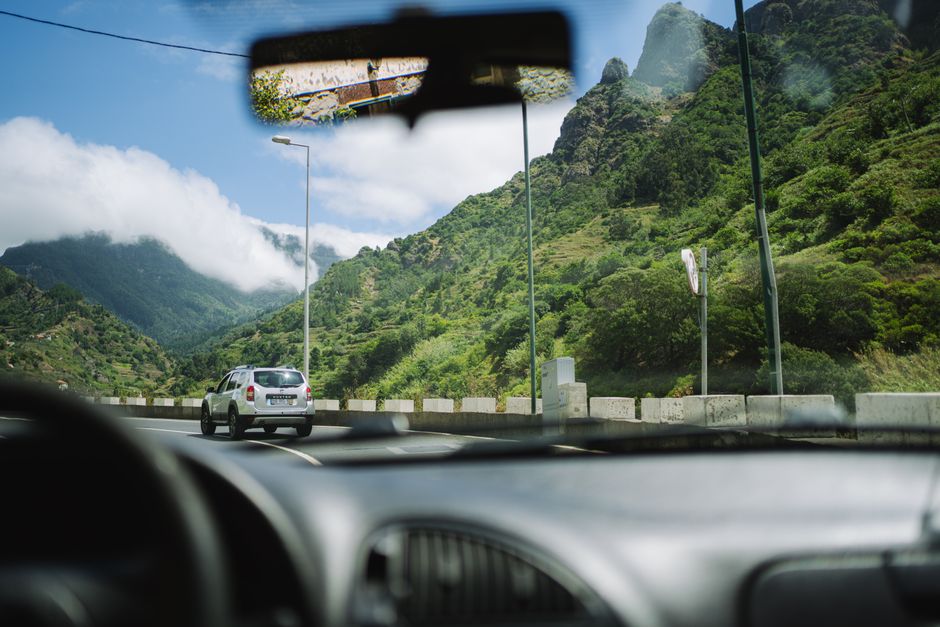 View from car window of a scenic drive through lush mountains on a sunny day.