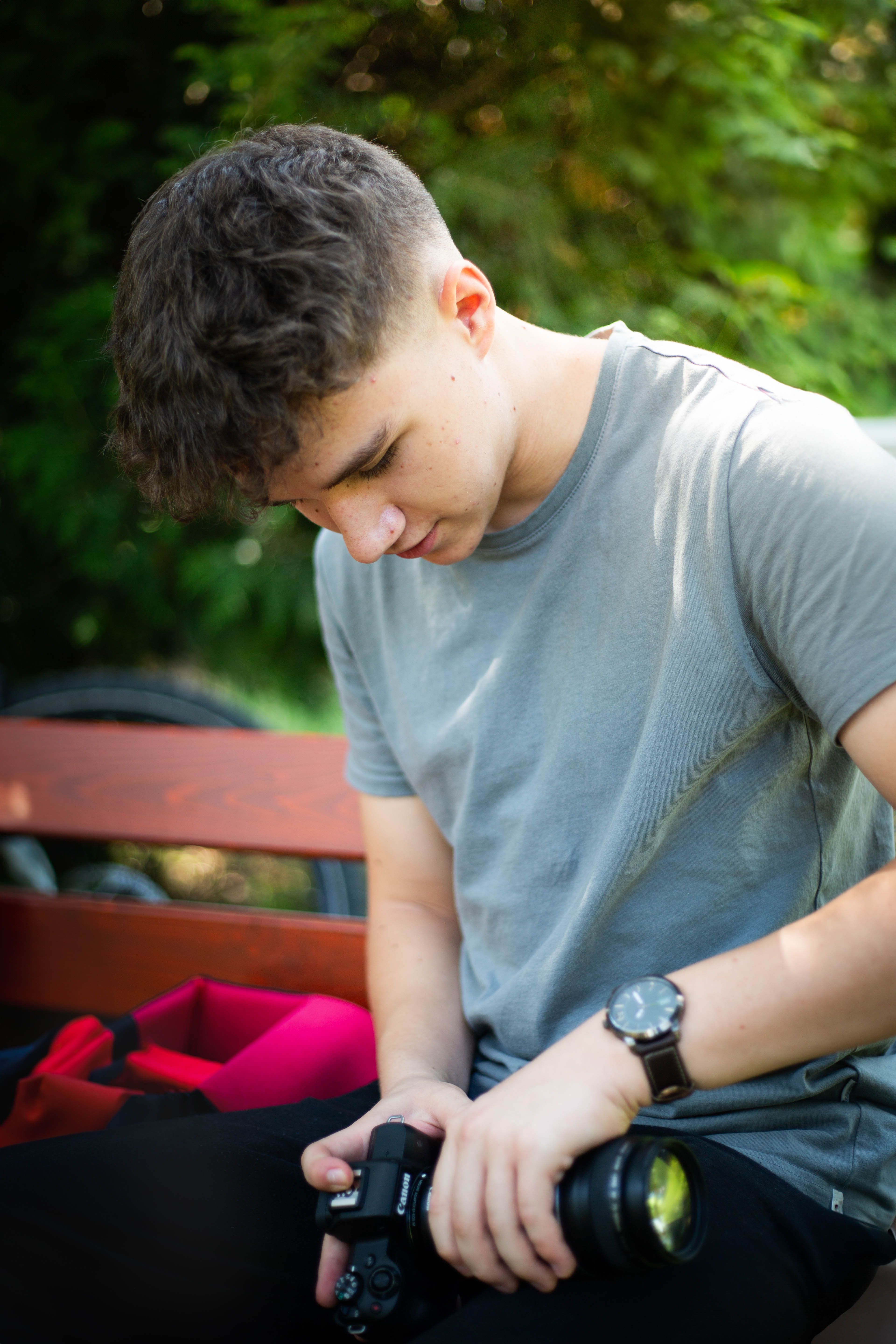 A young man prepares his camera on a bench under sunlight, capturing a peaceful moment.