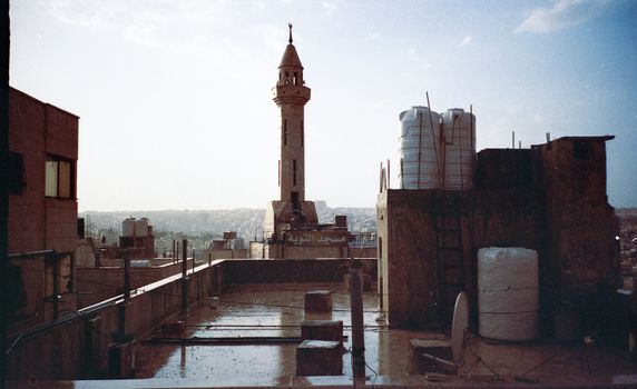 An urban rooftop scene in Amman, Jordan, featuring a prominent minaret under a clear sky.
