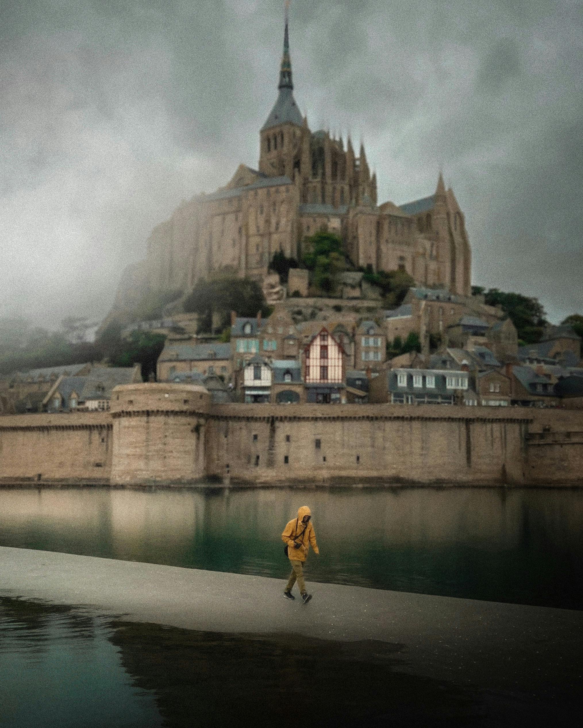 A majestic view of Mont Saint-Michel, France, shrouded in fog with a lone traveler in the foreground.