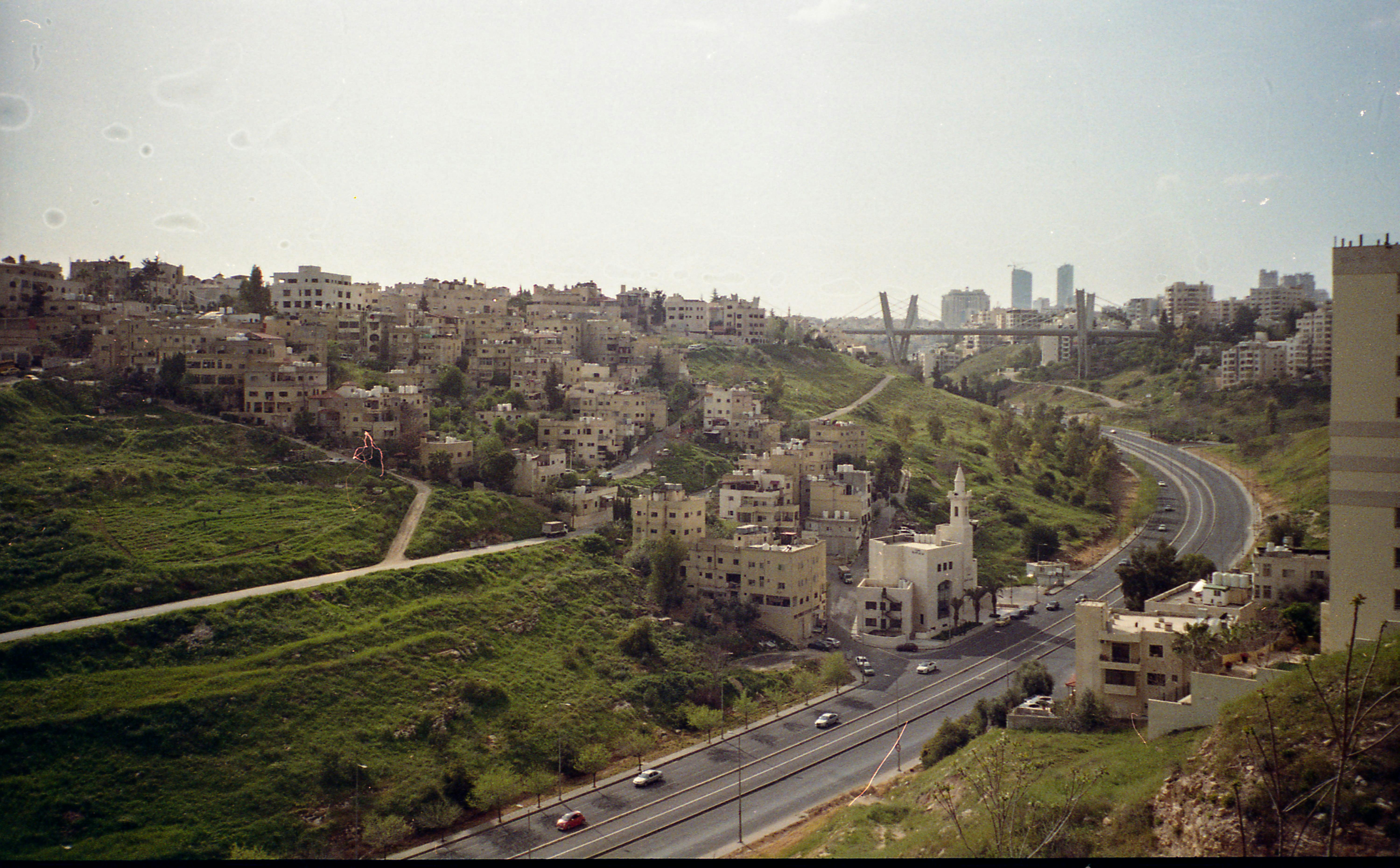 A scenic view of Amman, Jordan showcasing urban architecture with lush green hills and winding roads.