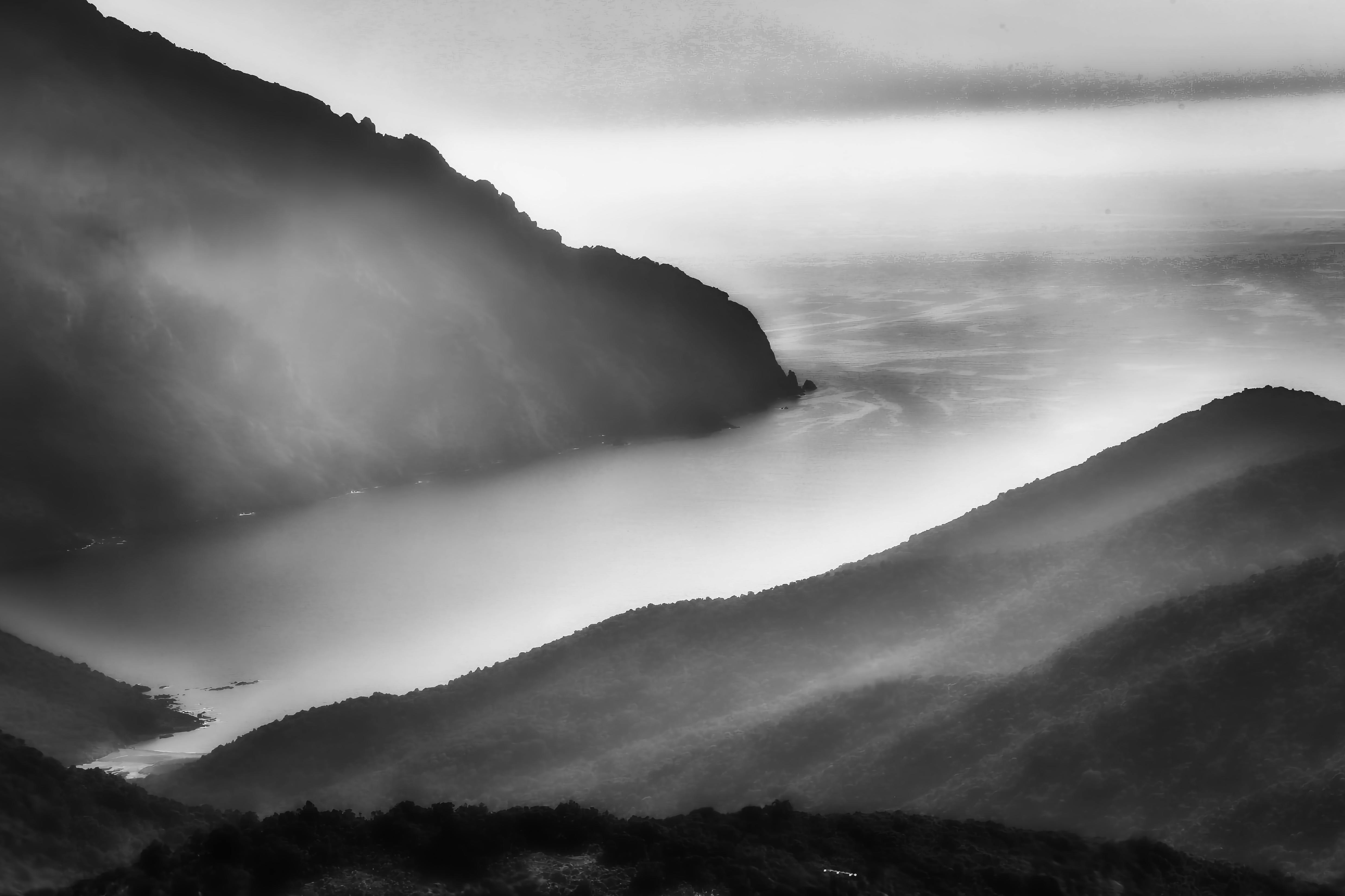 Black and white image of misty Corsica coastline, capturing serene mountain and sea views.