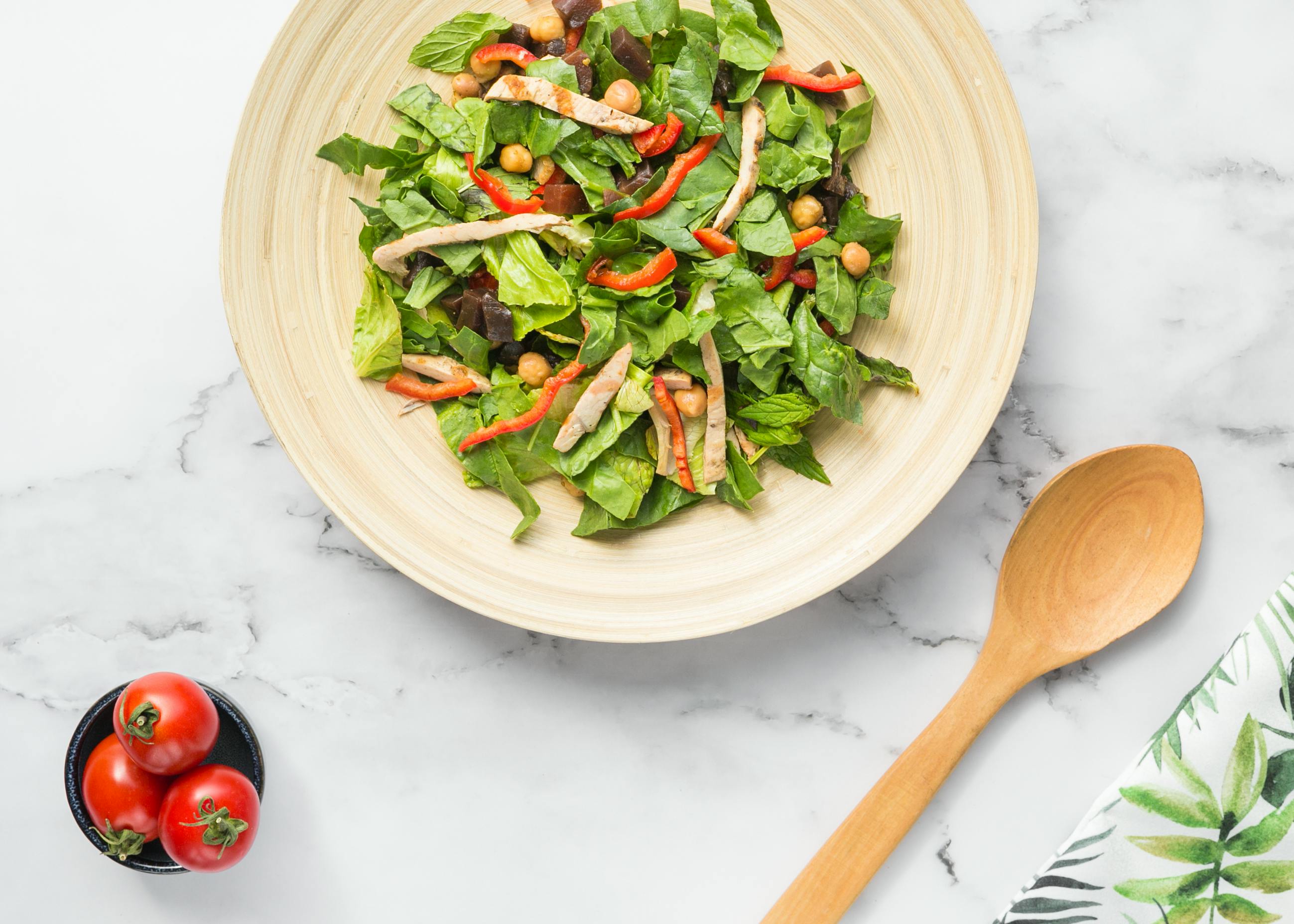 Colorful salad with leafy greens, tomatoes, red peppers, and chickpeas in a wooden bowl.