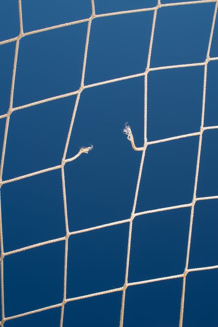Close-up view of a torn soccer net set against a vibrant blue sky, highlighting sports themes.
