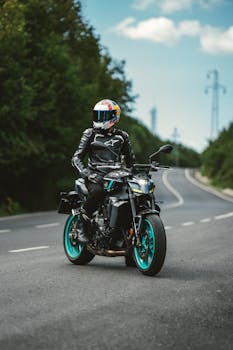 A motorcyclist on a scenic road with lush greenery, wearing protective gear on a stylish bike.