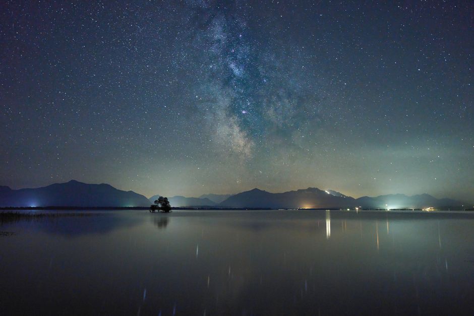 Beautiful Milky Way above Chiemsee Lake reflecting starlit sky and mountains at night.