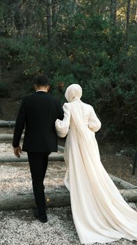 Bride and groom walking arm in arm outdoors, celebrating their wedding day in serene nature.