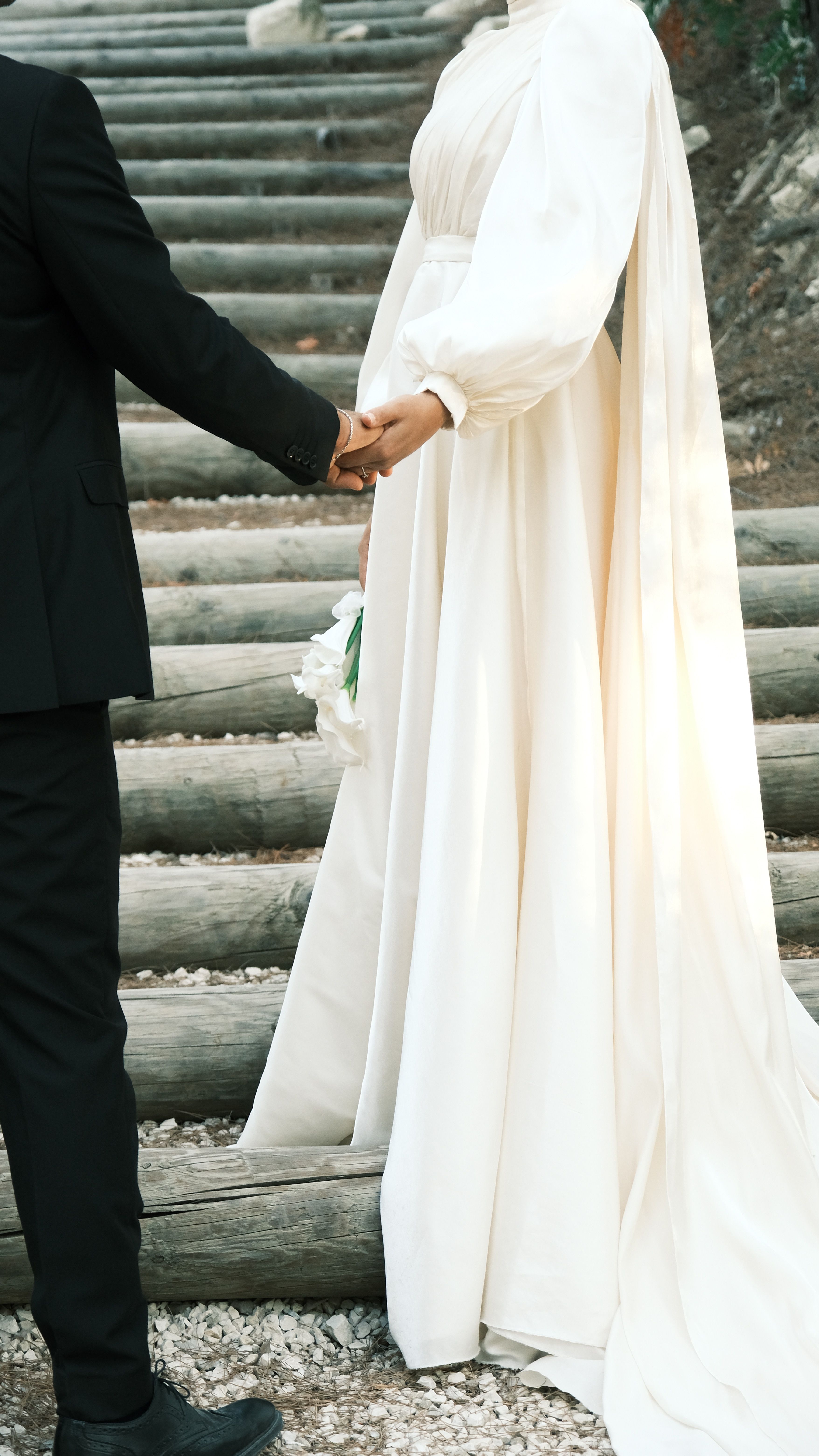 Bride and groom holding hands on a wooden staircase outdoors, showcasing love and elegance.