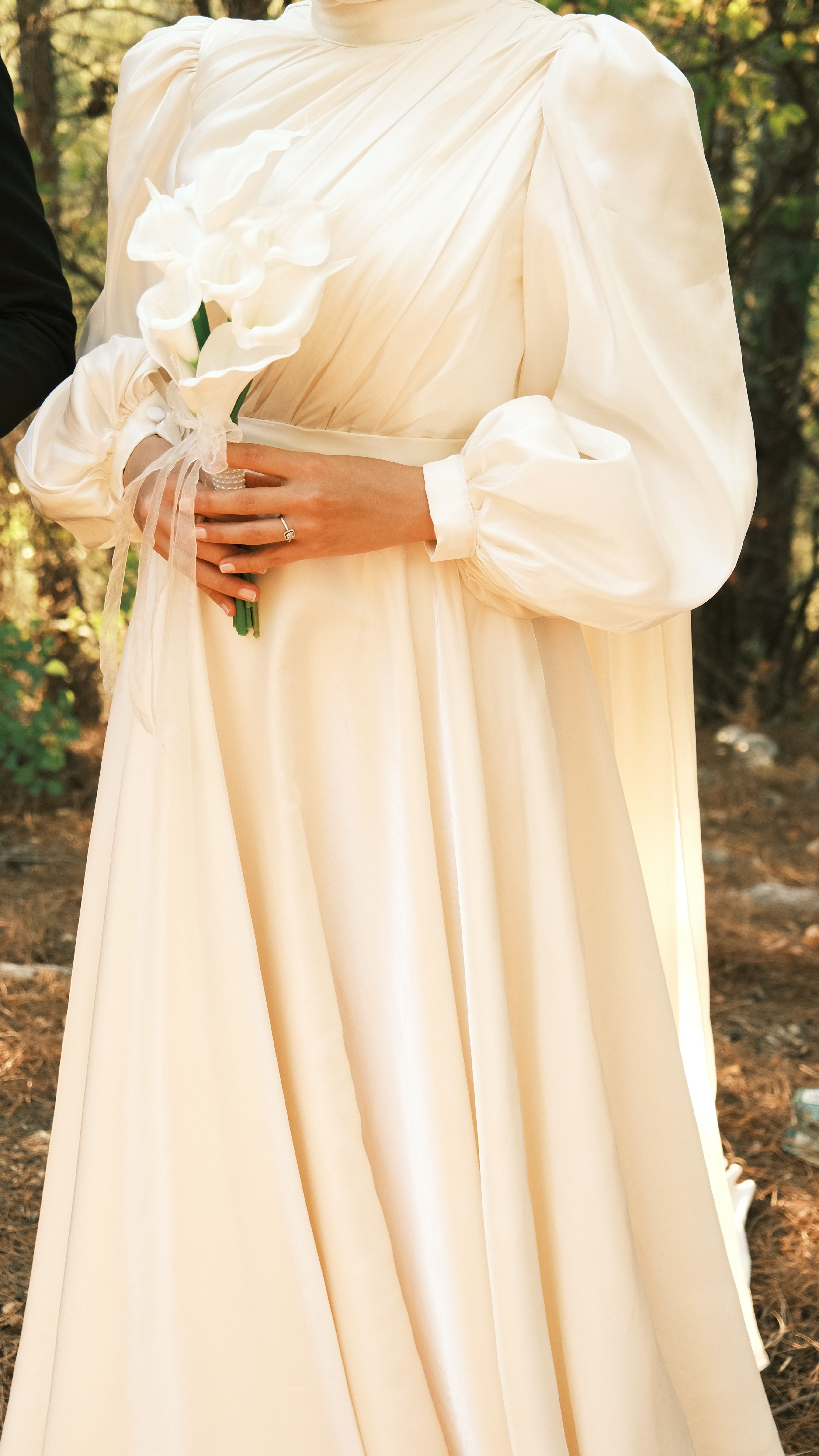 Bride holding a bouquet in an elegant dress outdoors in summer setting.