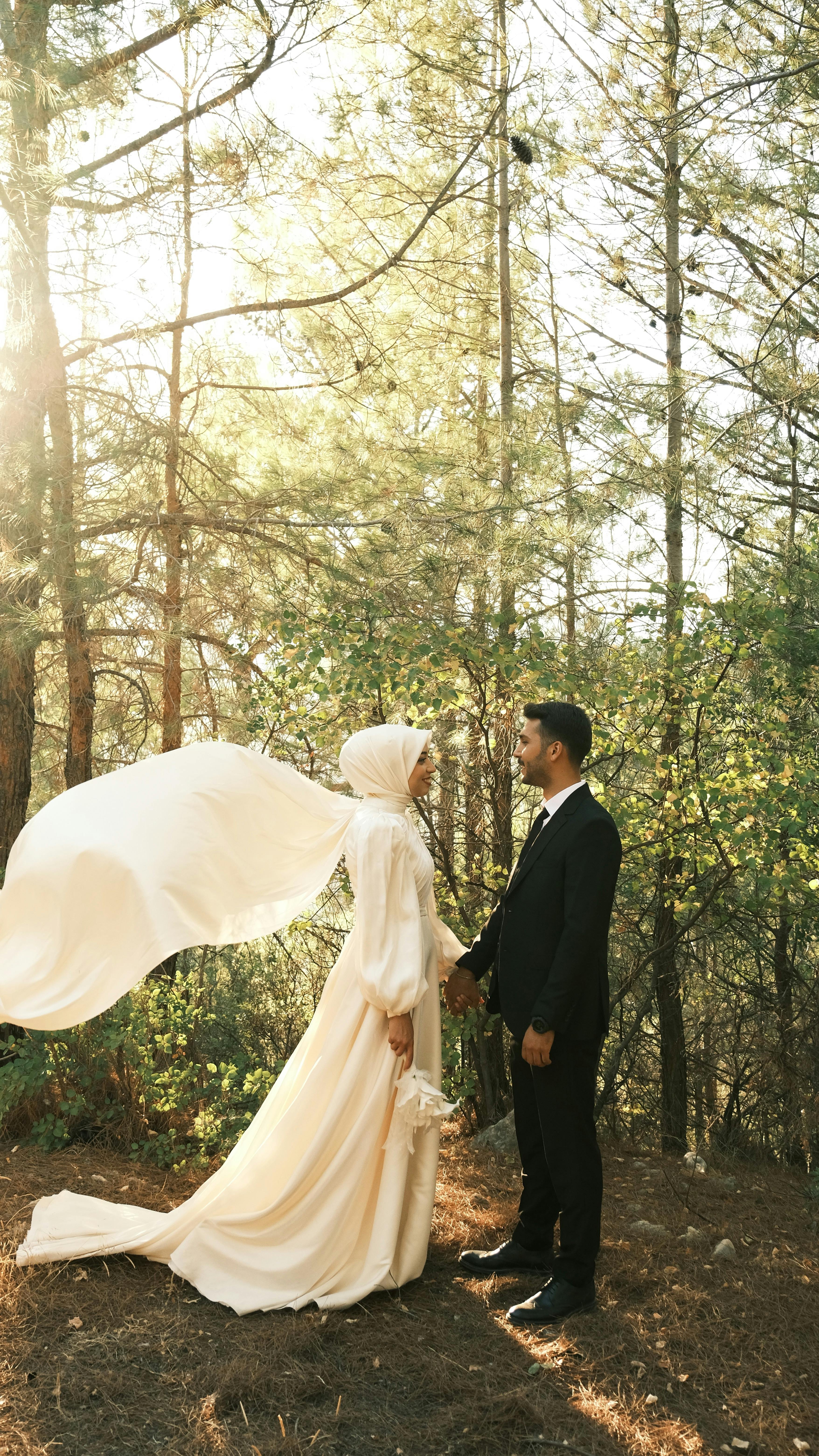 a bride and groom standing in the woods