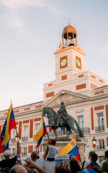People gather in Madrid's city center to protest, featuring flags and the iconic clock tower.