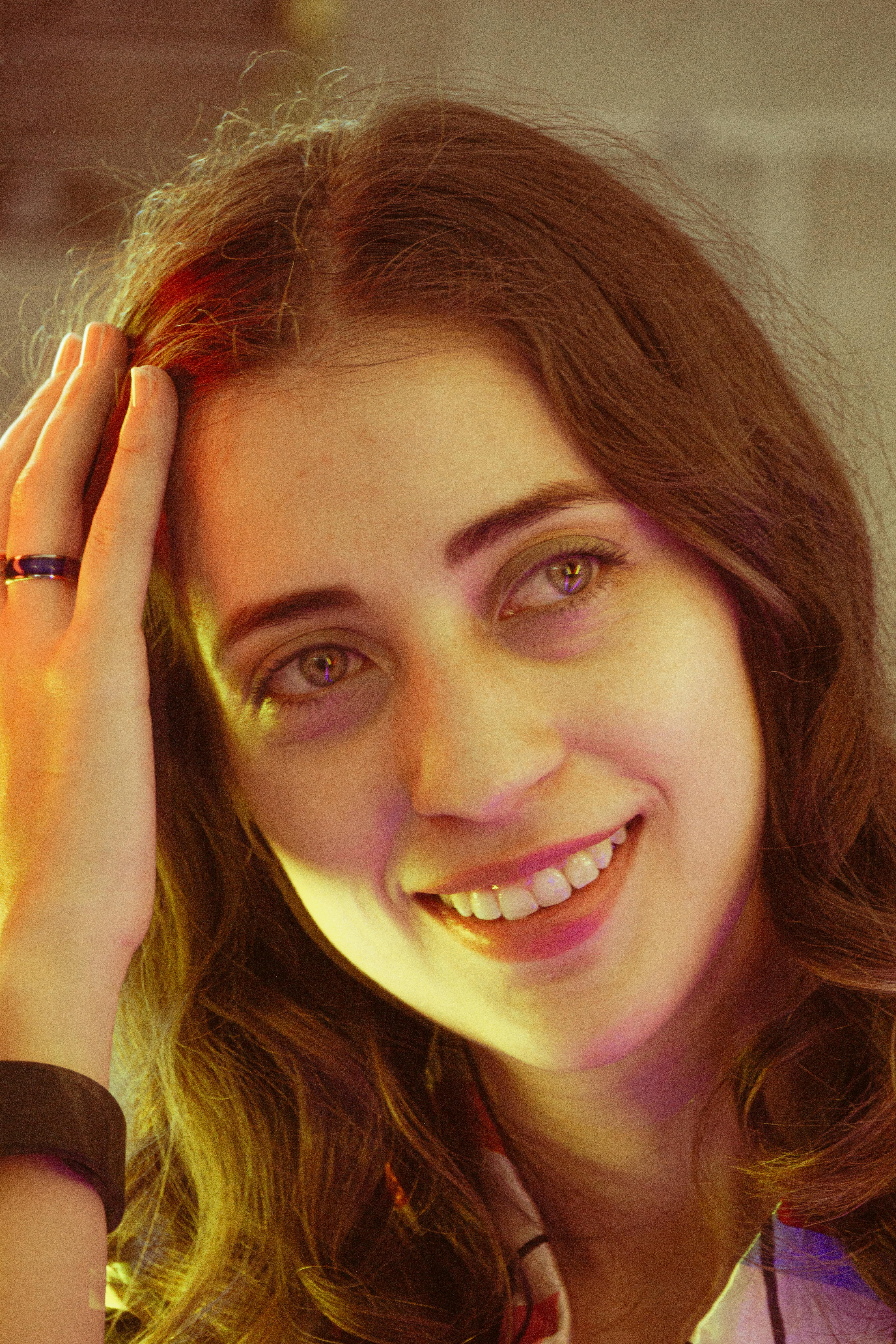 A young woman smiling warmly under colorful indoor lighting, conveying a joyful mood.