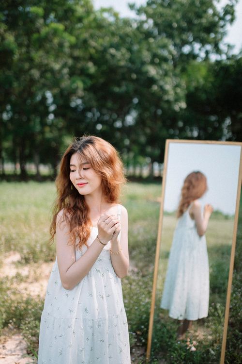 Free Young woman in white dress enjoying nature, reflected in the mirror. Summer vibes. Stock Photo
