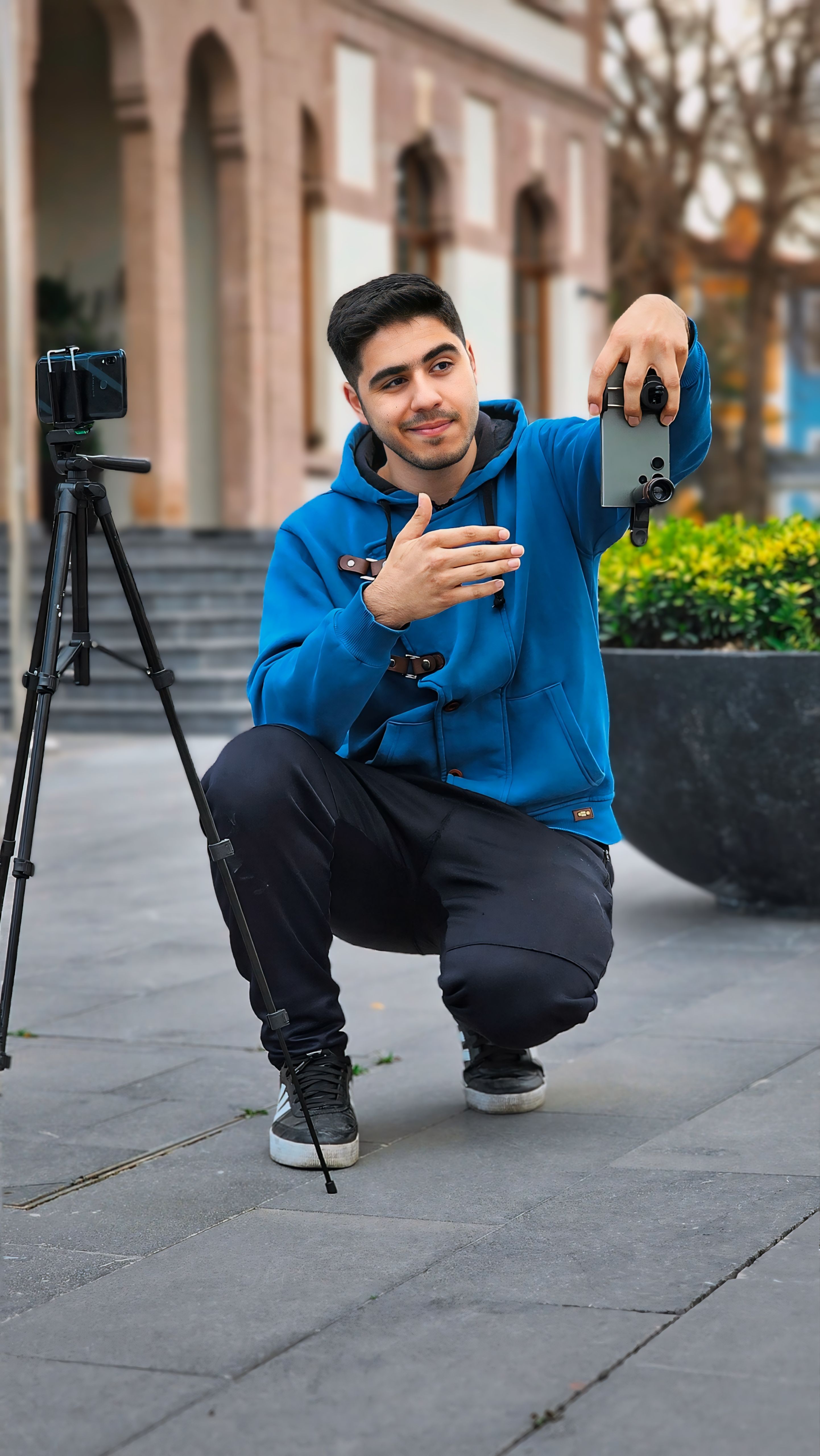 Young man adjusts camera on tripod in urban setting, displaying focus and creativity.