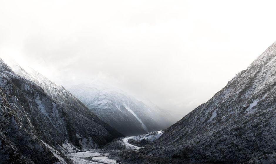 Breathtaking view of a snowy mountain valley in New Zealand with misty peaks and a winding river at dusk.