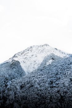A serene winter landscape with a snow-covered mountain peak under a bright sky.