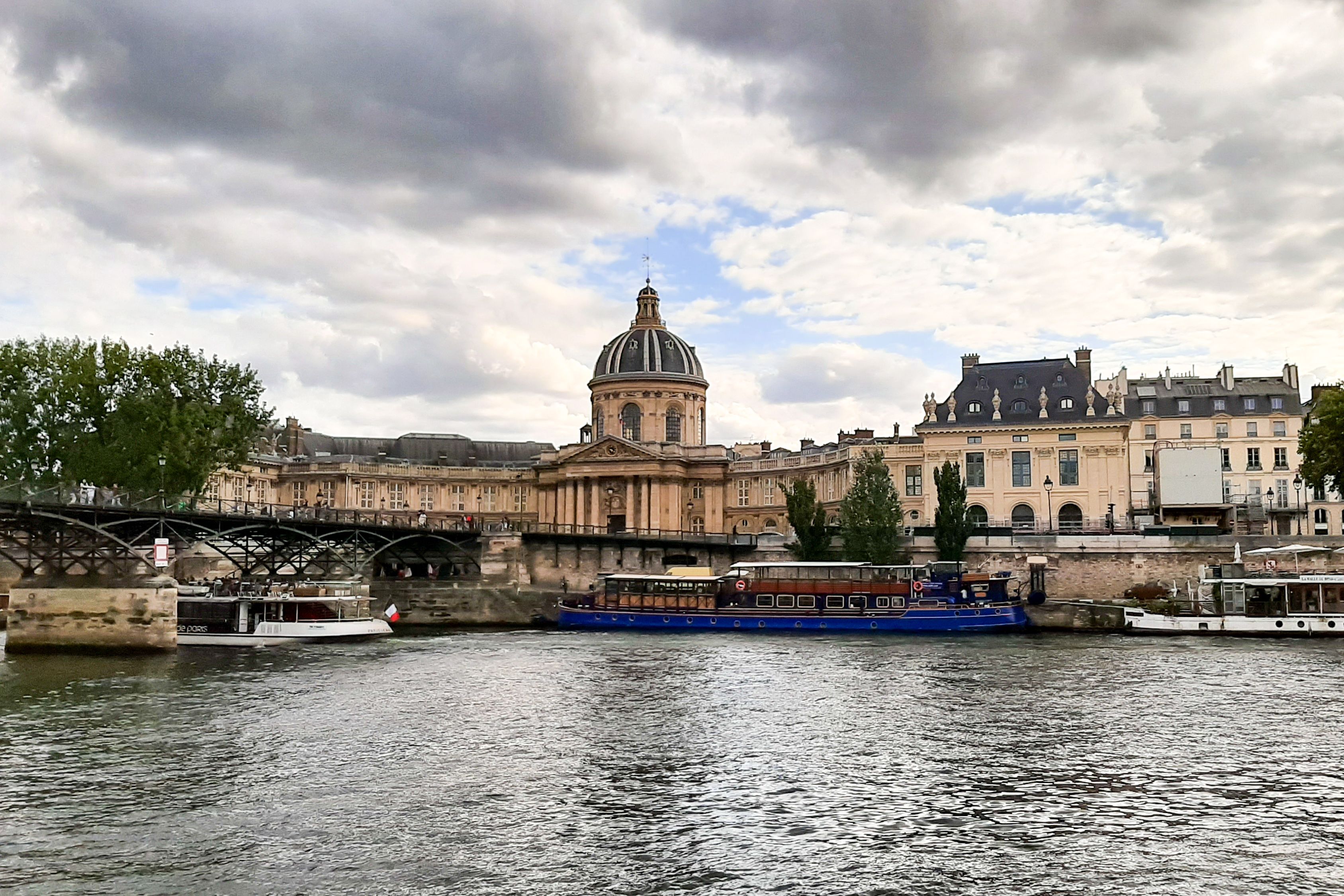 Scenic view of iconic Paris architecture along the Seine River on a cloudy day.
