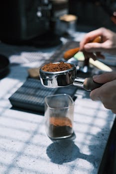 Hands preparing espresso with freshly ground coffee in an indoor kitchen setting.