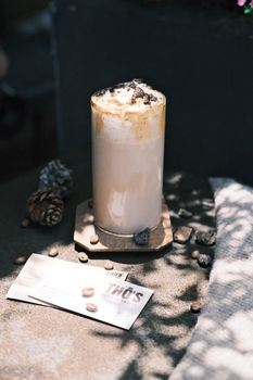 A tall iced coffee topped with whipped cream and chocolate, surrounded by coffee beans.