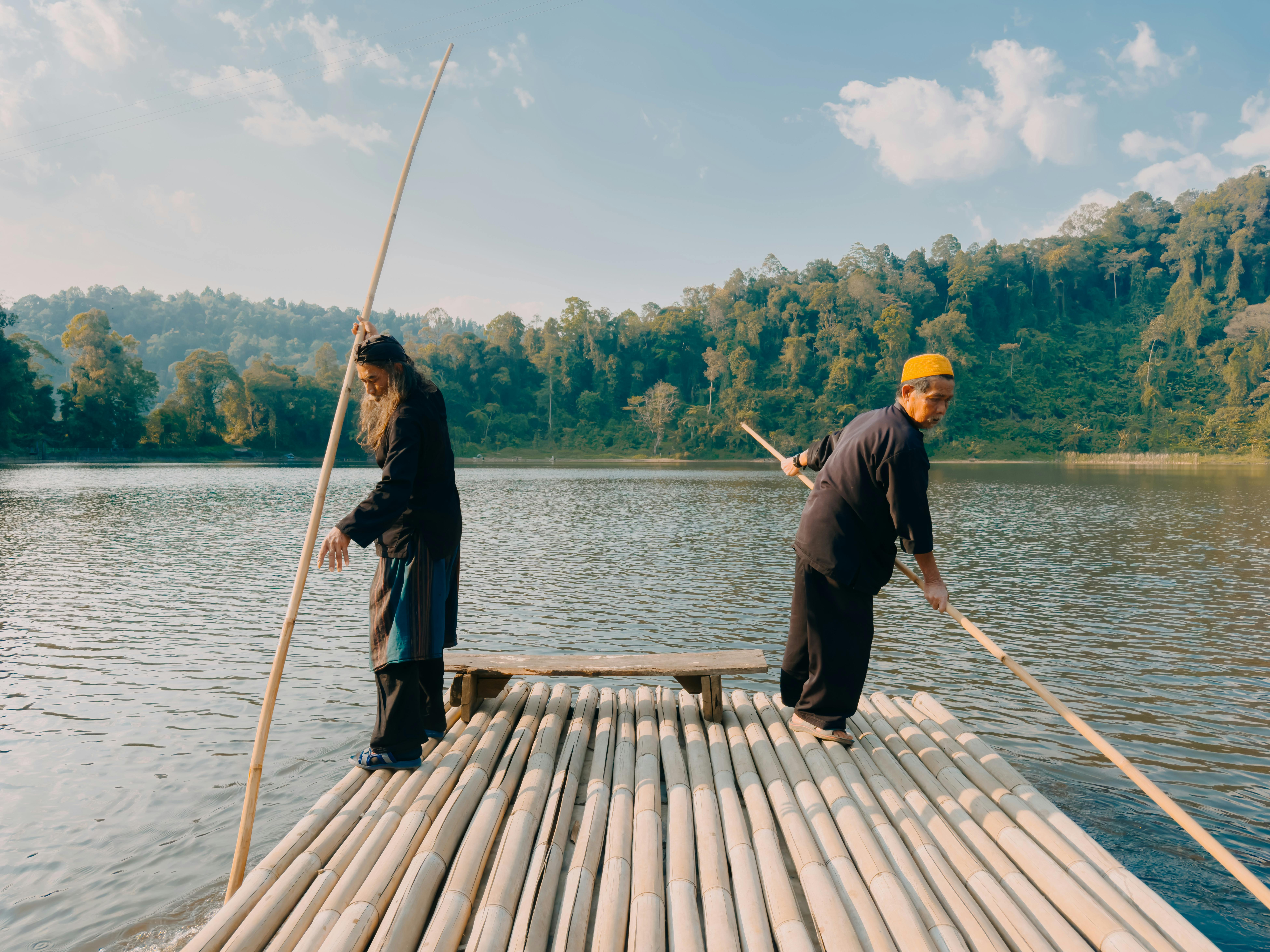 Two people on a bamboo raft enjoying the serene lake setting in West Java, Indonesia under a clear blue sky.