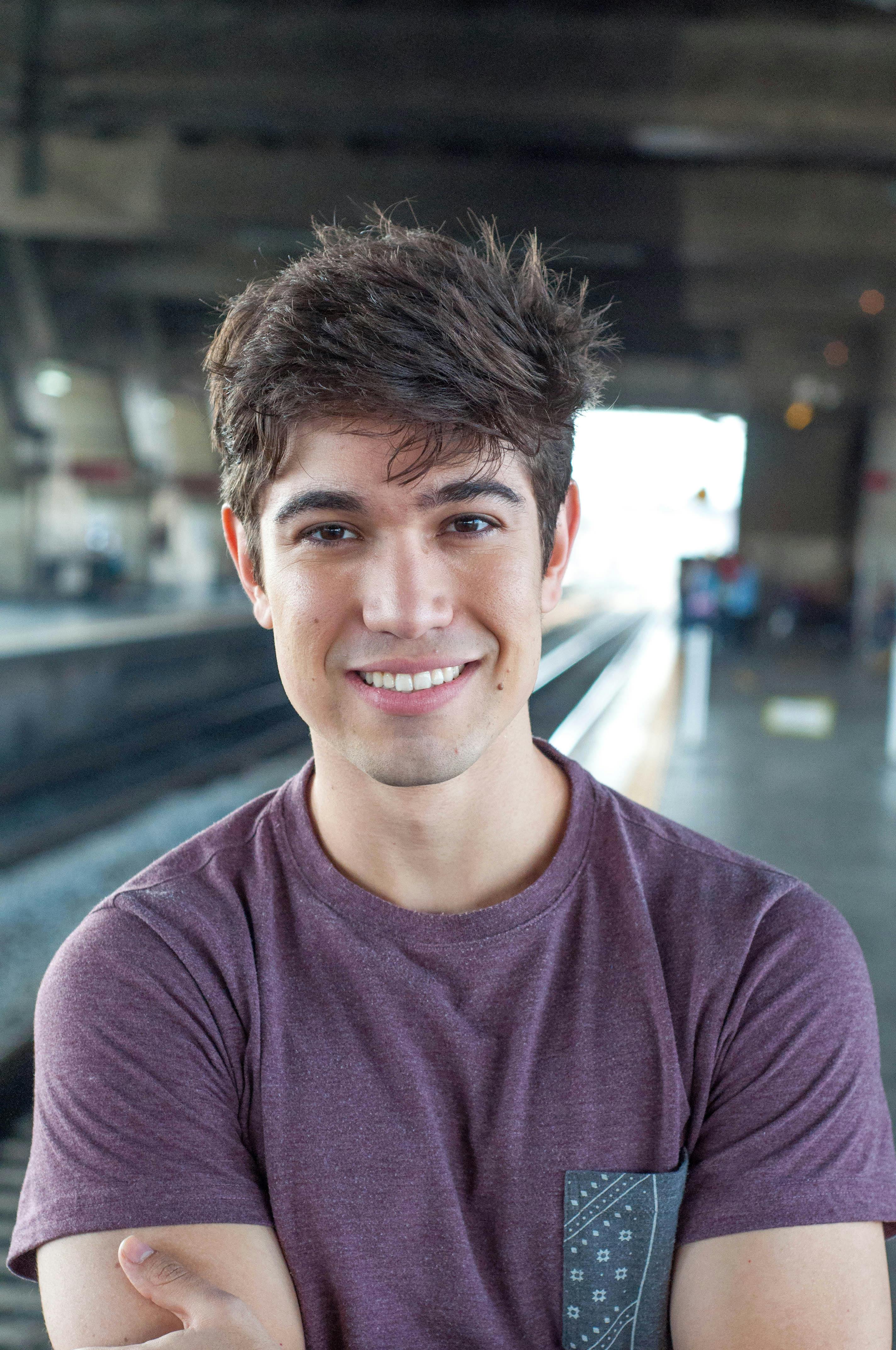 Portrait of a young man smiling confidently at a train station platform, embodying casual fashion and leisure.