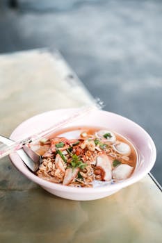 Delicious Thai noodle soup served in a pink bowl with chopsticks on a table.
