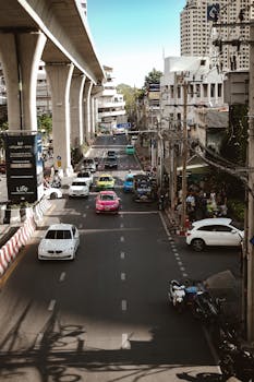 Vibrant street view of Bangkok with cars and elevated railway.