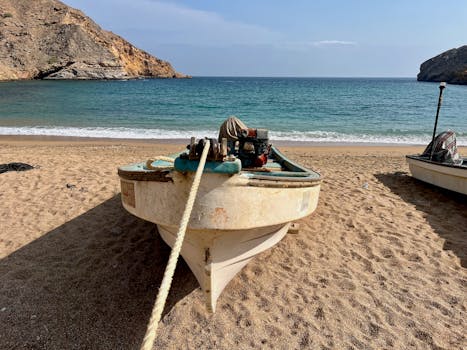 Tranquil view of a boat on the sandy beach of Bandar Al Khairan, Oman, with rocky coastline and blue sea.