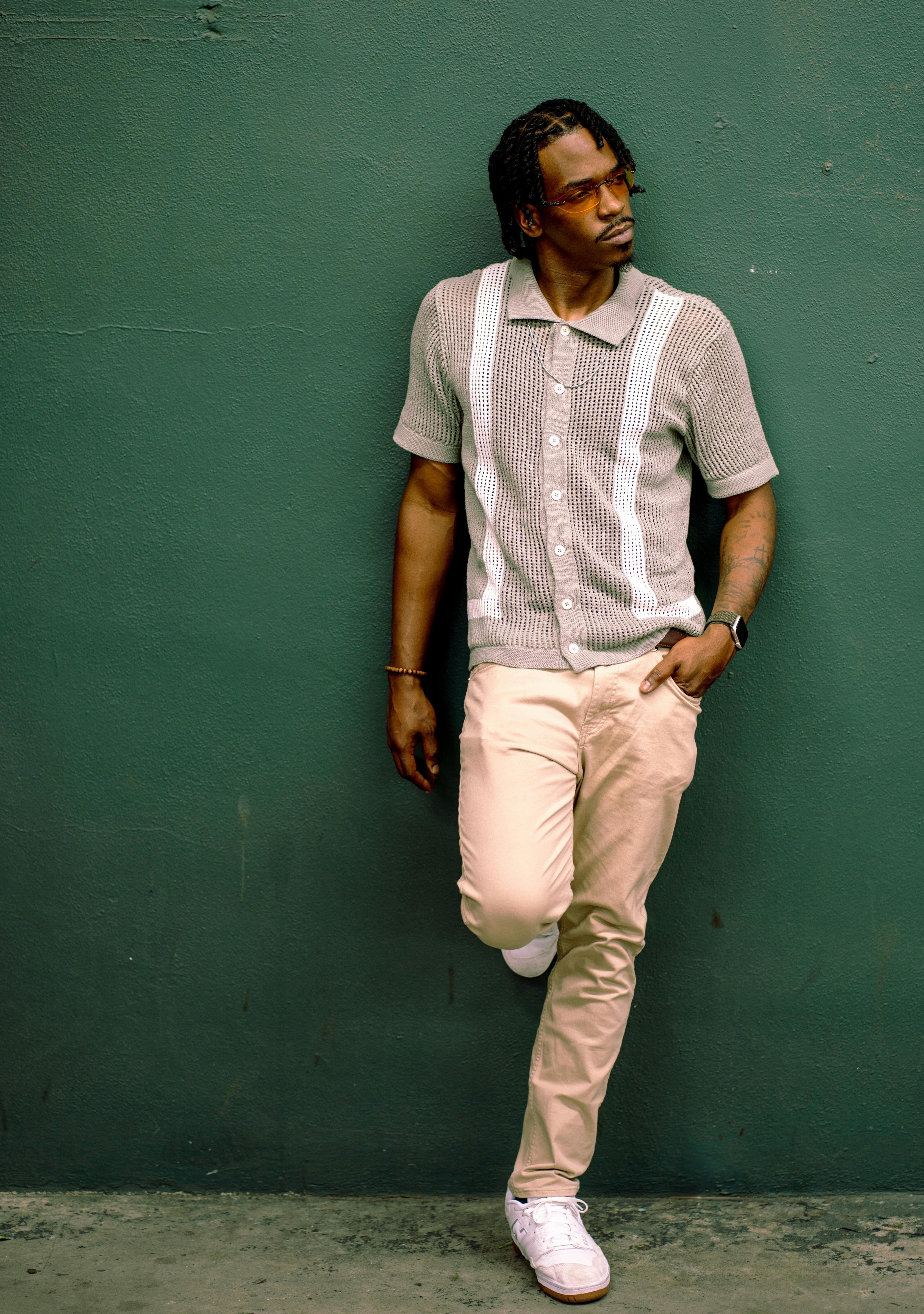 Fashionable man in casual attire leaning on a green wall outdoors.