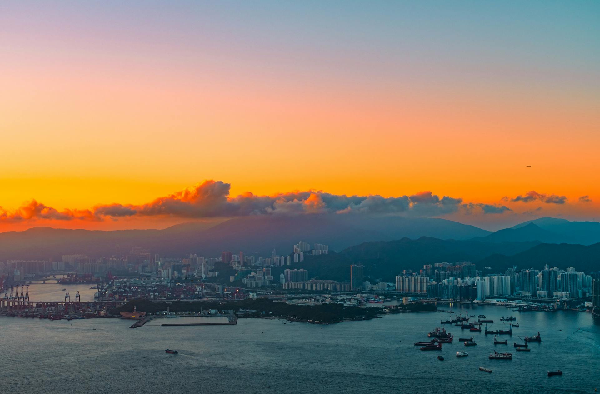 Aerial view of Hong Kong cityscape at twilight, featuring brightly colored sunset over the skyline and harbor.