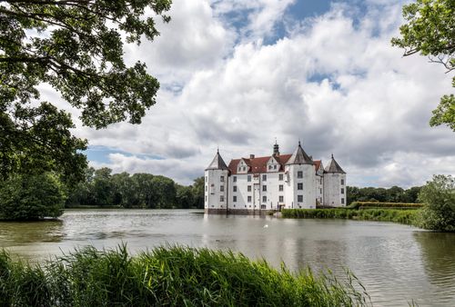 Free Beautiful view of Glücksburg Castle reflected in a serene lake under a bright summer sky. Stock Photo