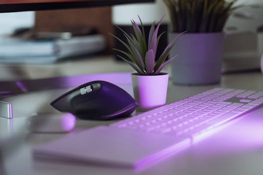 Stylish home office workspace featuring keyboard, mouse, and potted plant under purple illumination.