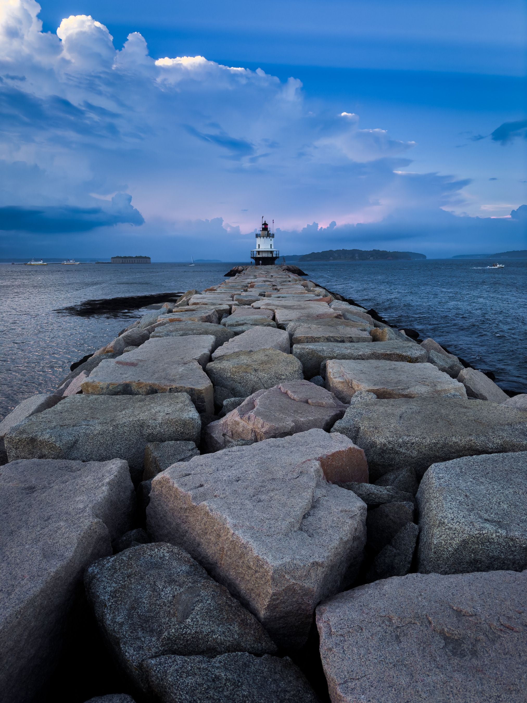 A lighthouse sits on a rocky shore with a cloudy sky · Free Stock Photo