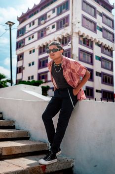 Young man with sunglasses poses stylishly in front of colorful building.