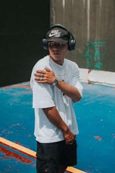 A stylish young man wearing headphones and a cap in an urban sports setting on a bright day.