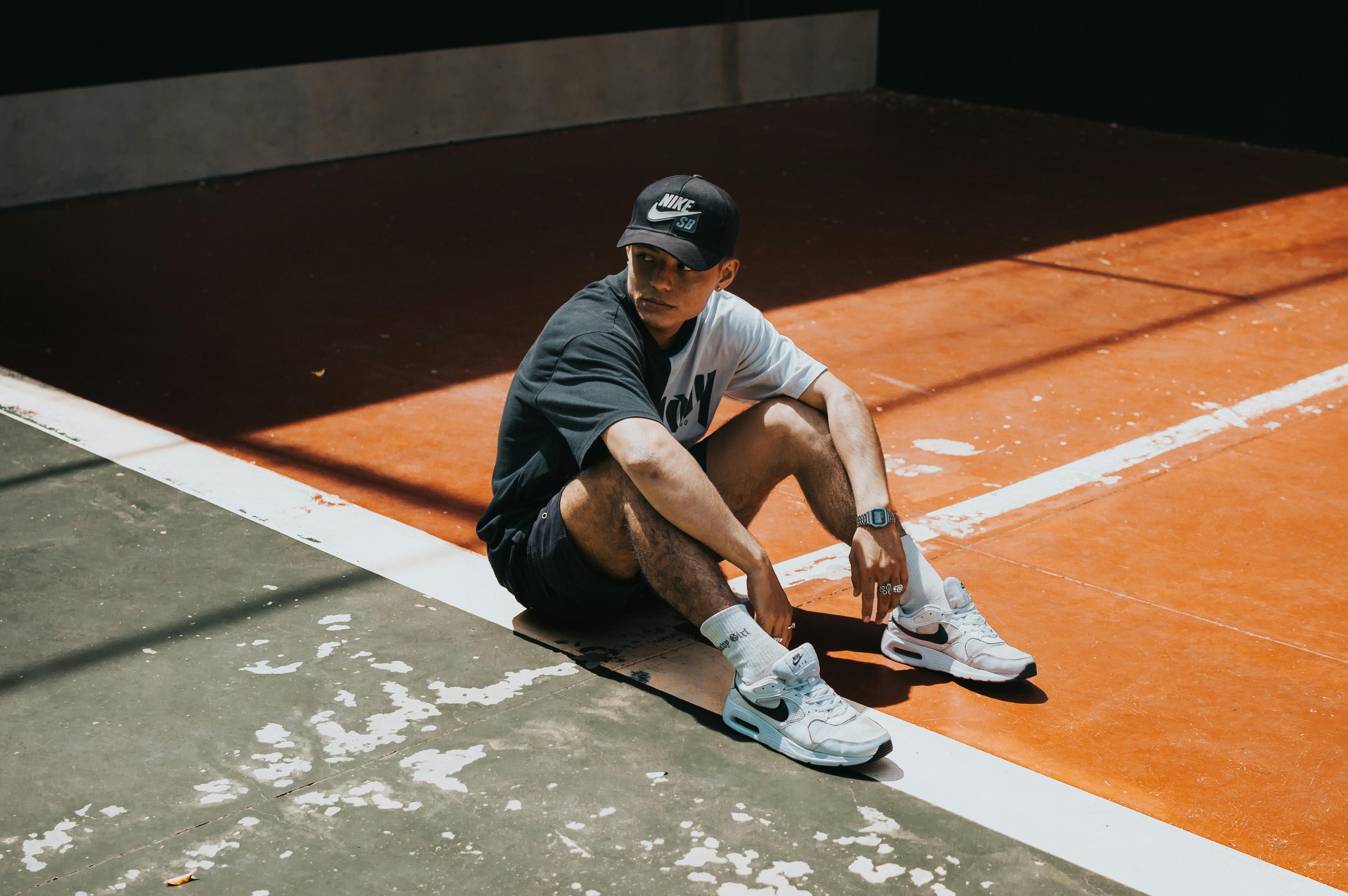 Man in sporty attire seated on an outdoor court, showcasing a relaxed pose.