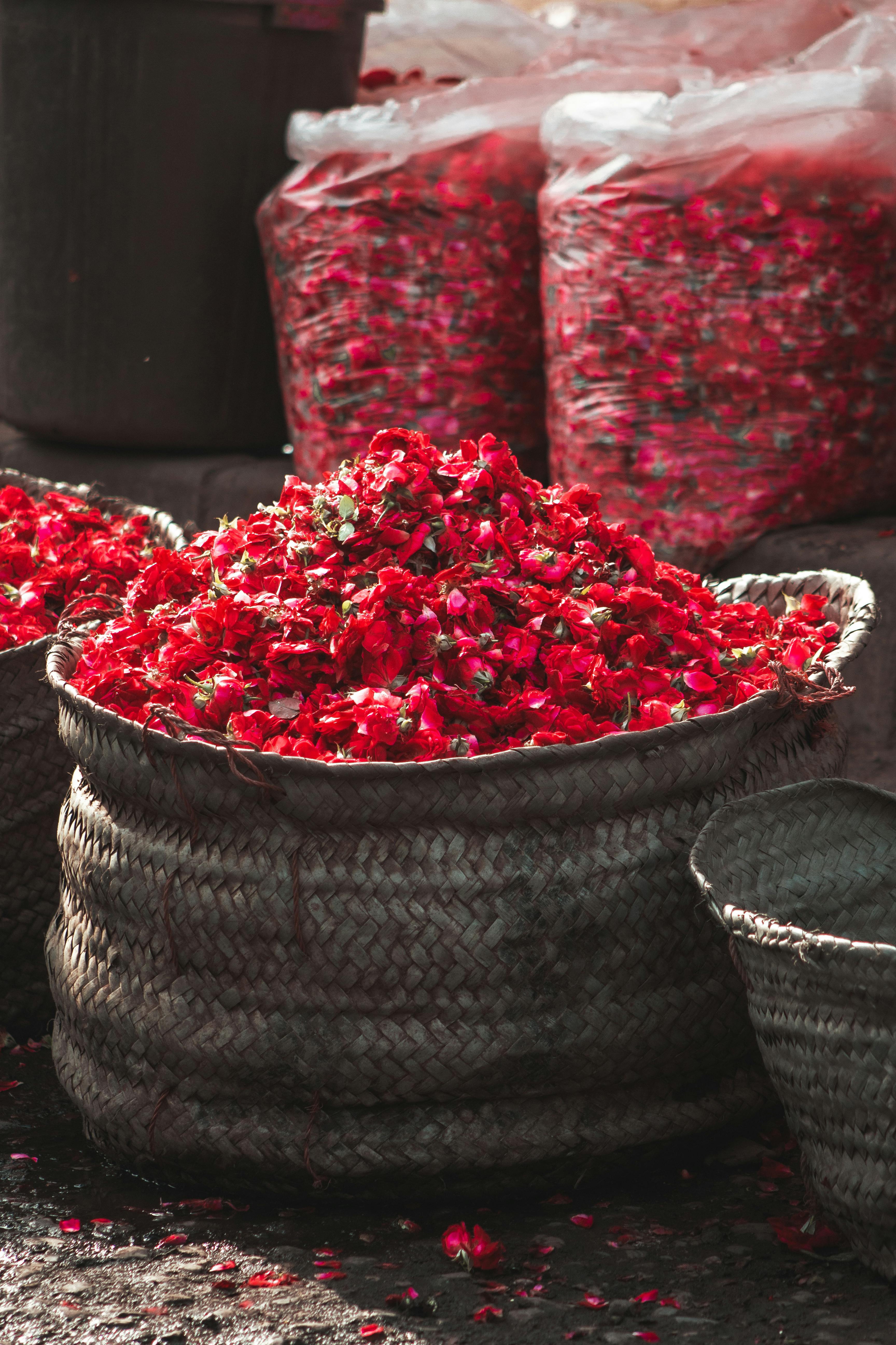 Colorful display of fresh red rose petals in a traditional basket at a Karachi market.