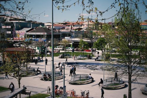 Free A bustling urban park with people walking and relaxing, surrounded by city buildings and trees. Stock Photo