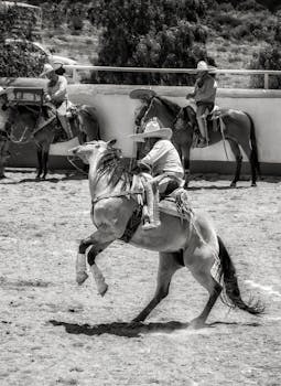Black and white photo capturing cowboys in action at a lively rodeo event.