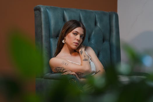 Portrait of a stylish woman with tattoos sitting elegantly indoors.