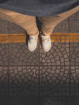 Top view of white sneakers on a textured, patterned pavement with warm lighting.