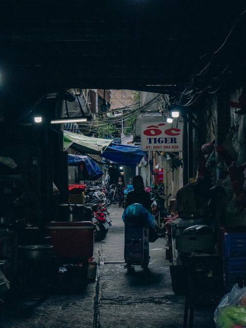 Free A bustling urban alley at dusk in Vietnam, filled with motorbikes and a vendor pushing a cart. Stock Photo