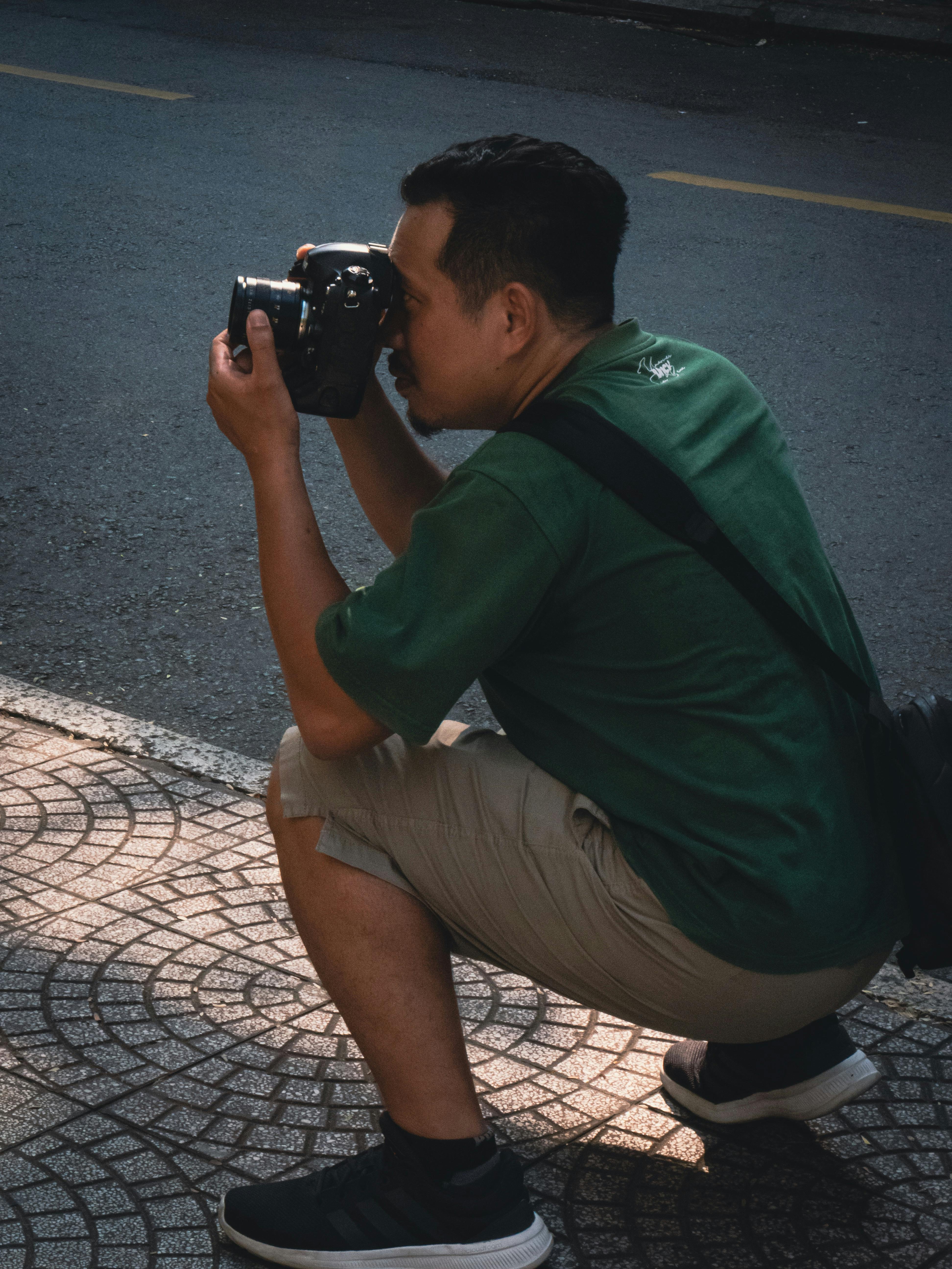 Man in green shirt taking photos on city street, showcasing urban lifestyle.
