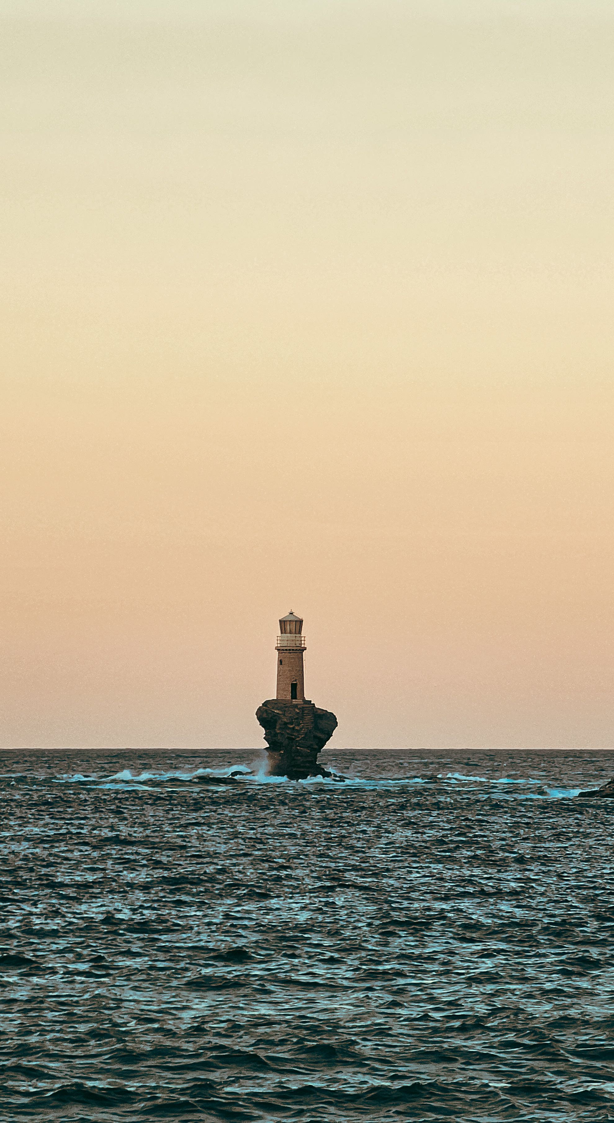 solitary white lighthouse above a calm ocean coast at golden sunset